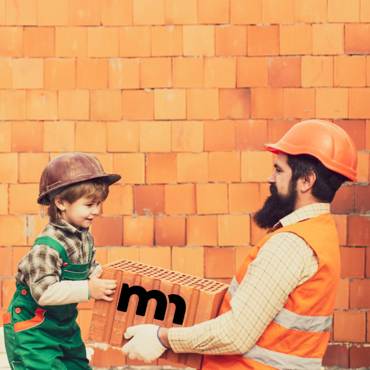 Man and child wearing hardhats while holding a cement block in front of a home under construction